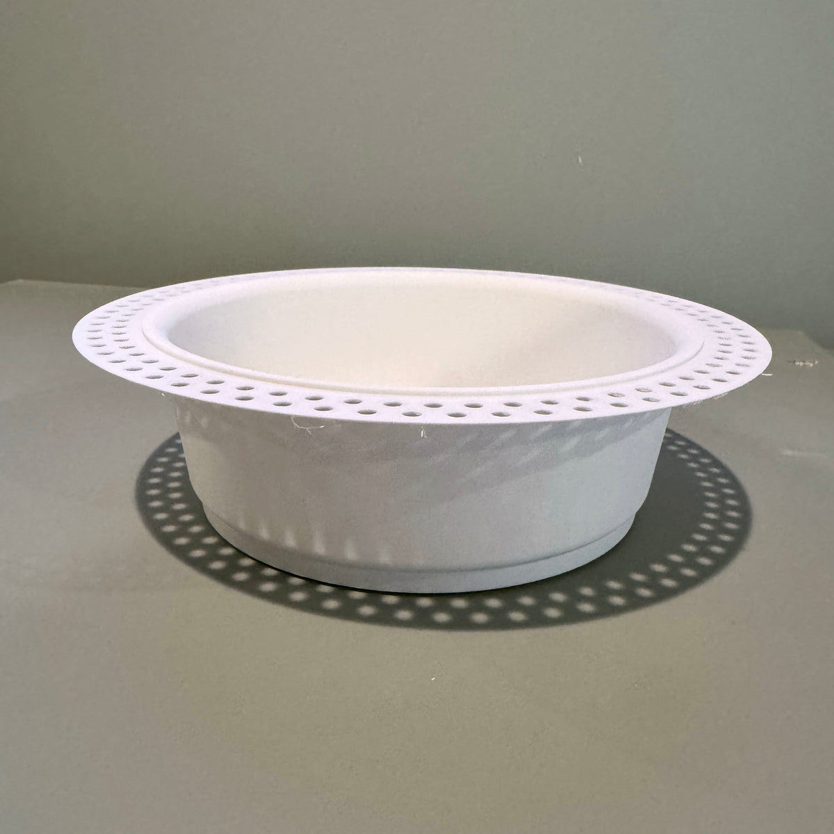 Side view of the white round trimless drywall mount showing its recessed body and perforated flange.