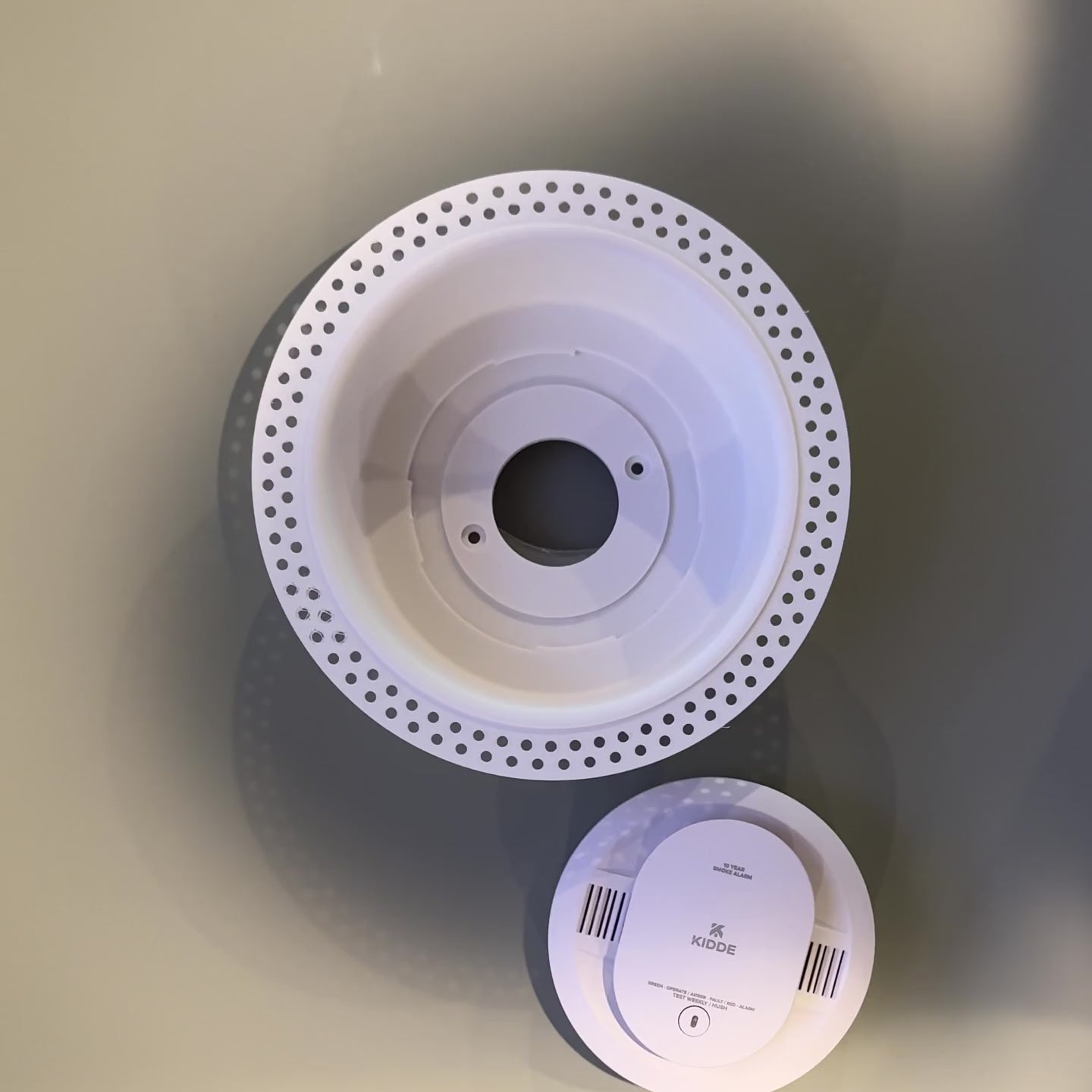 Fit reference showing a detector device placed into the white round trimless drywall mount; device not included.
