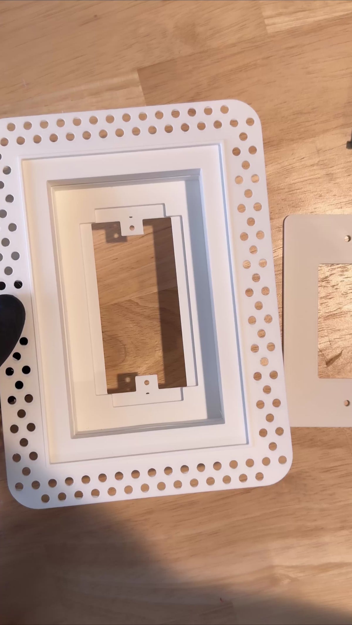 Gloved hands fitting the wall-plate insert and removable cover into a white trimless low-voltage enclosure