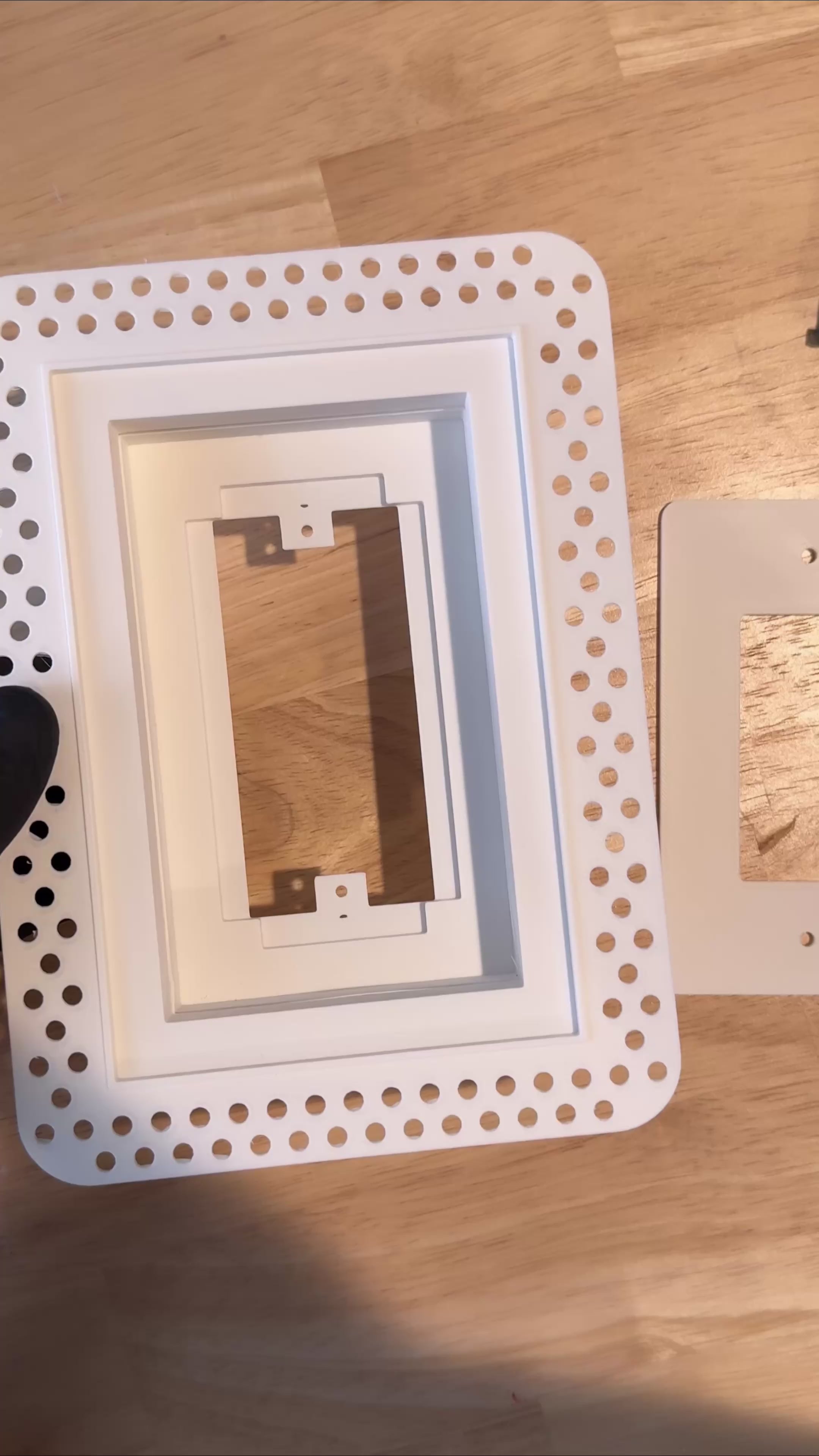 Gloved hands fitting the wall-plate insert and removable cover into a white trimless low-voltage enclosure