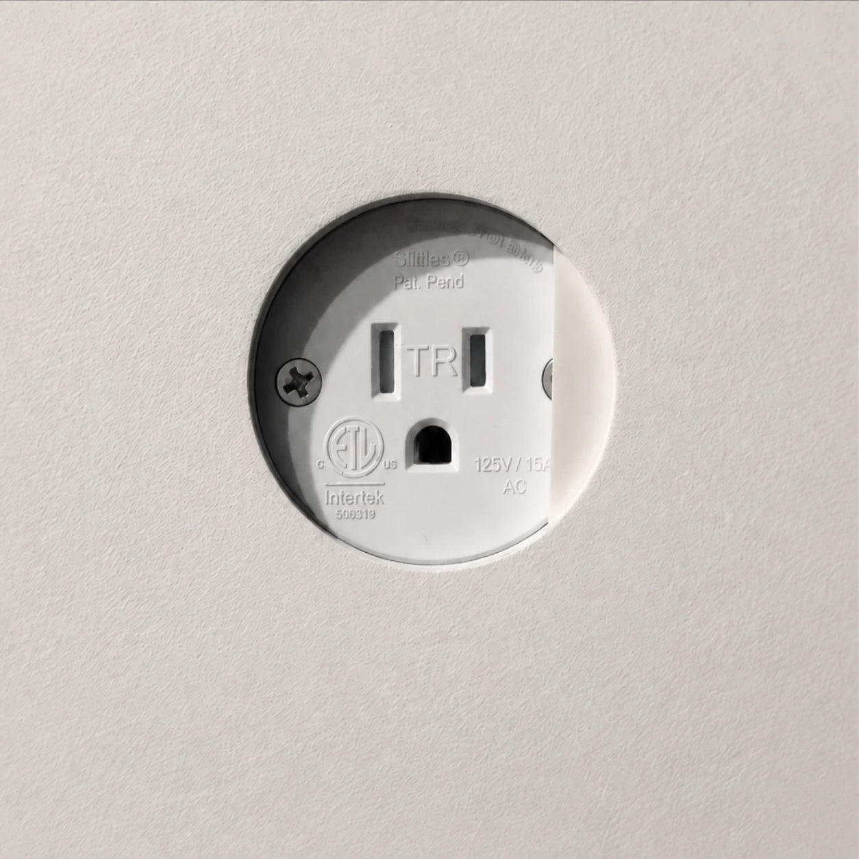 Round white electrical receptacle with a sliding cover installed flush in a painted wall