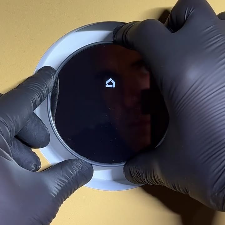 A wall being painted yellow around a trimless round mount before gloved hands install a smart thermostat