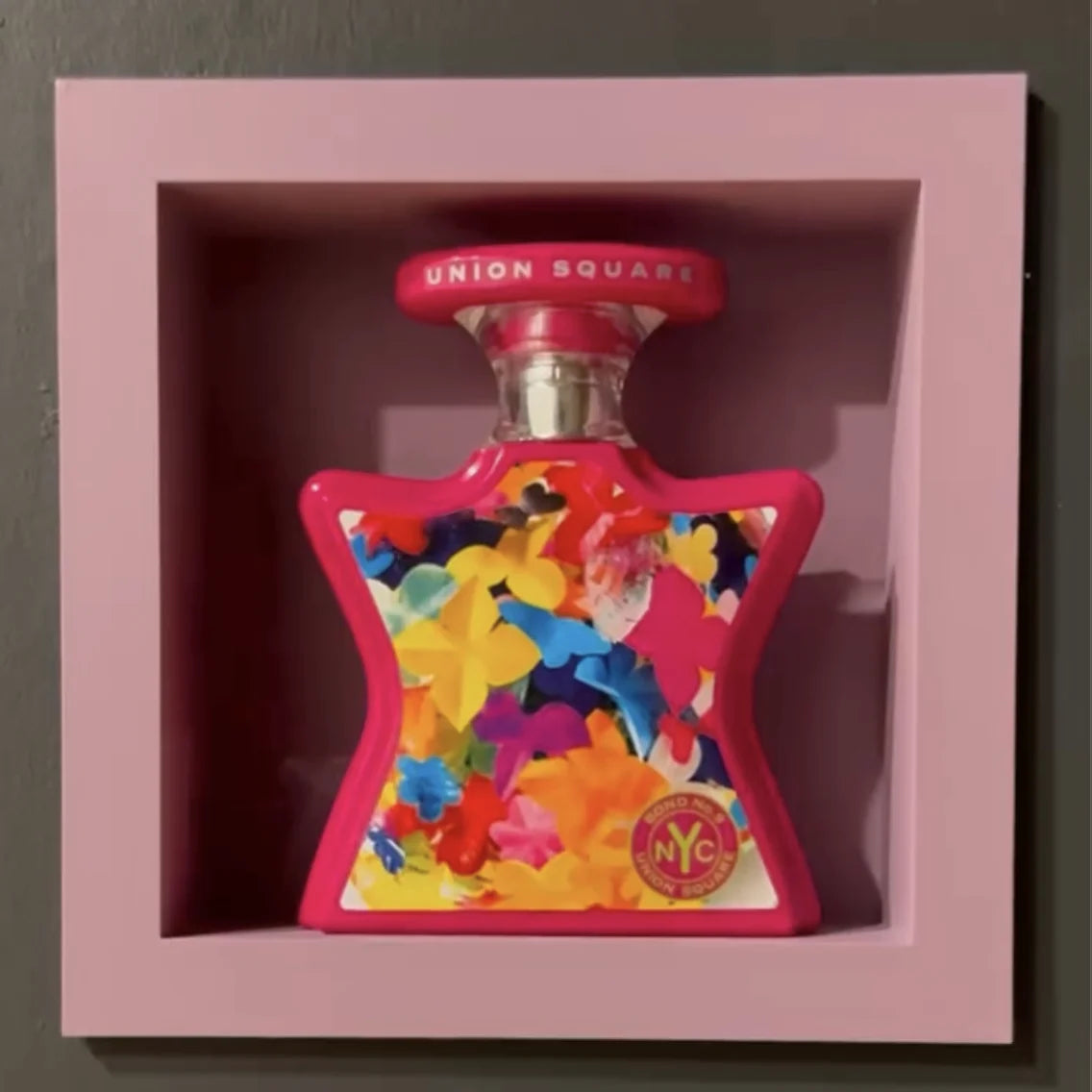 Pink square recessed niche with a clean visible frame holding a colorful perfume bottle